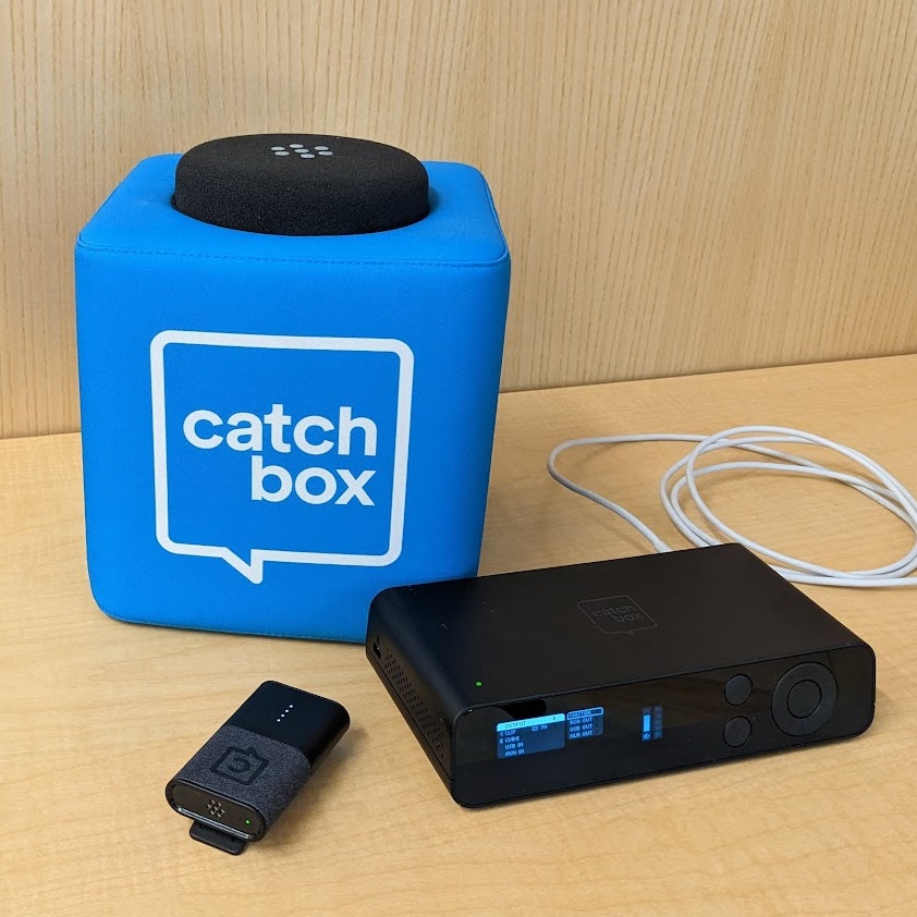 A Blue cube with rounded and padded edges, with a black protrusion, labeled 'Catch Box'. Below it is a small rectangular microphone with a clip and a control box with LED screen.